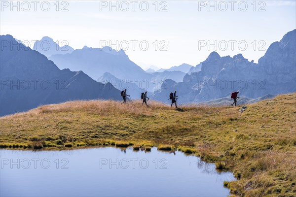 Four hikers on the Carnic High Trail, small mountain lake, Carnic Main Ridge, Carnic Alps,