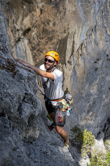 A climber with helmet and safety equipment scales a steep rock face, alpine climbing with rope,