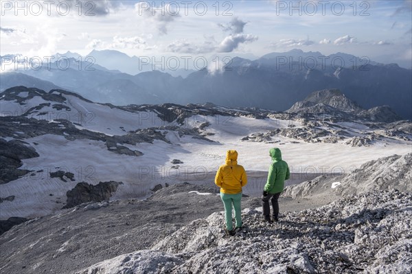 High alpine landscape, snowfields and rock, Two hikers look down into the valley from the