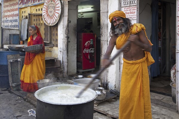 Hindu man wearing red bindi on forehead stirring food in huge pot for the needy in Udaipur,