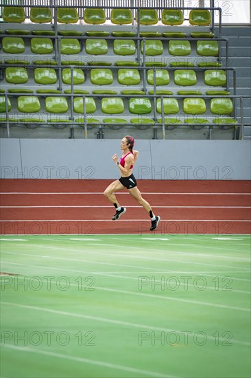 Lone runner trains on the running track of an empty stadium with green rows of seats, Glaspalast,