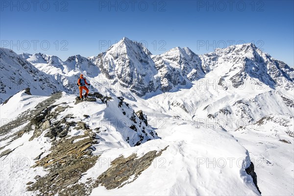 Mountaineer standing on a ledge in front of snow-covered mountains, summit of Madritschspitze,