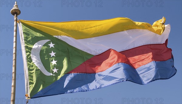 The flag of the Comoros flutters in the wind, isolated against a blue sky