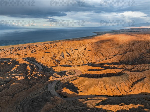 Riverbed runs through a landscape of eroded hills, badlands at sunset, Issyk Kul Lake in the