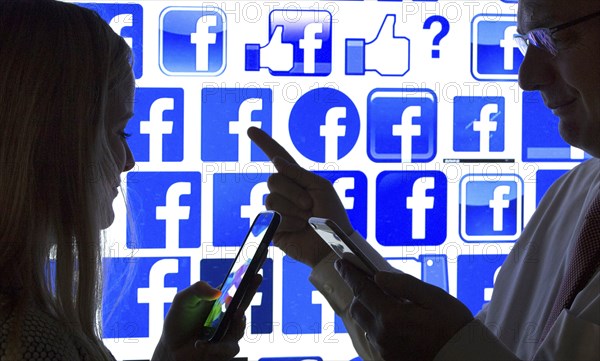 Woman and a man with smartphones in front of Facebook logo, 12.01.2016