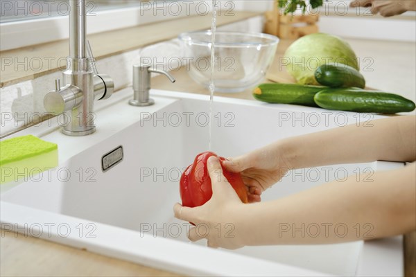 Closeup view of hands of kid washing bell pepper in the sink