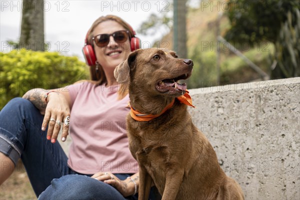 Pretty woman sitting on a concrete staircase, listening to music, accompanied by her dog. Selective