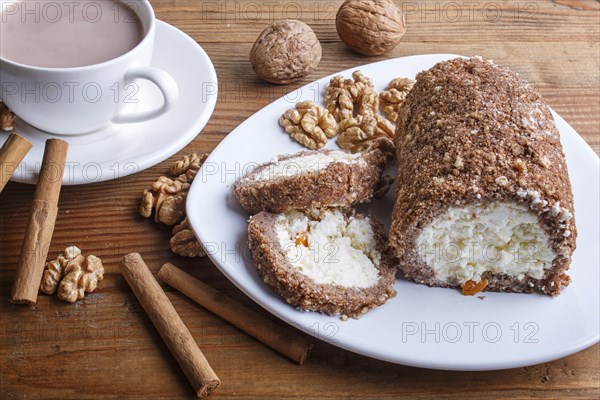 Roll cake with curd and walnuts isolated on brown wooden background, close up