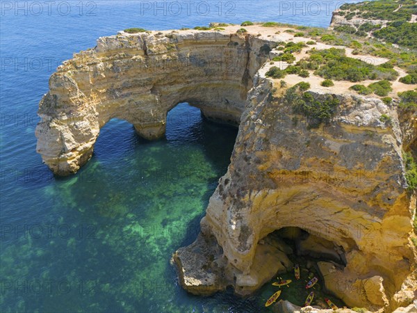 Large rock formations with natural arches on the coast, near water with canoes, aerial view, Praia