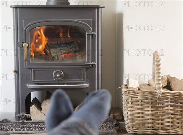 Roaring domestic household wood burning ClearView stove fire log basket with feet up in foreground