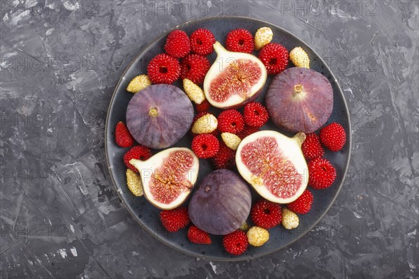 Fresh figs, strawberries and raspberries on blue ceramic plate on black concrete background. top