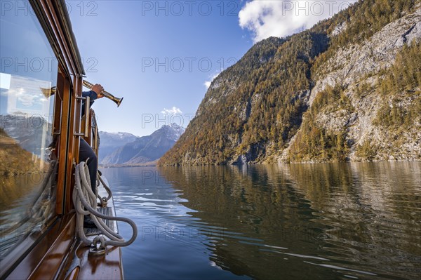 A trumpet is played on the echo wall of a tourist boat, Königssee, autumnal mountain landscape