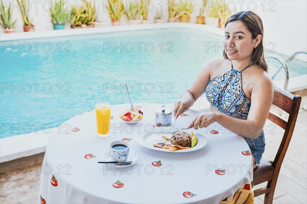 Smiling girl having breakfast near the swim pool. Woman on vacation having breakfast near swimming