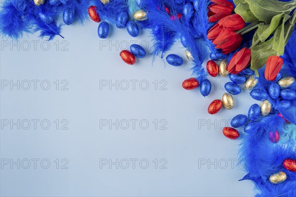 Colourful composition with blue feathers, red tulips and Easter eggs on a blue background