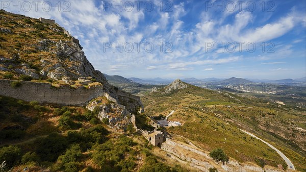 A view over a winding mountain path leading to ancient ruins with a sweeping vista, Archaic Castle,