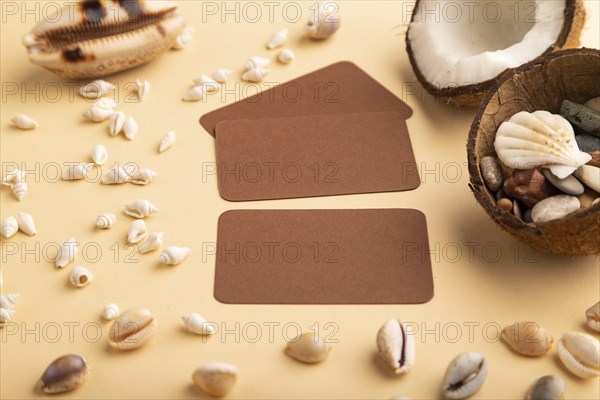 Brown paper business card with coconut and seashells on orange pastel background. Side view, copy