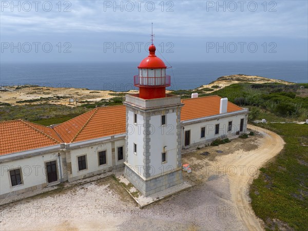 Close-up of a lighthouse and a neighbouring building overlooking the sea under a cloudy sky Aerial