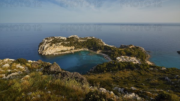 Coastal landscape with rocky cliffs and clear blue water under a sunny sky, Anthony Quinn Bay,