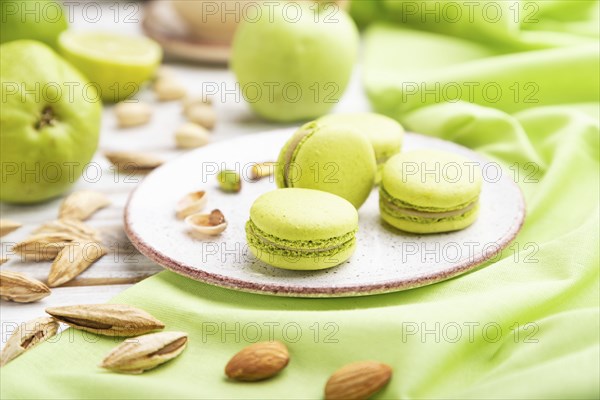 Green macarons or macaroons cakes with cup of coffee on a white wooden background and green linen