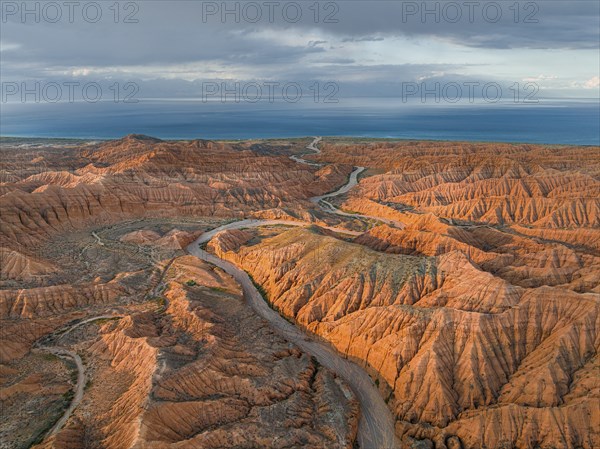 Riverbed runs through a landscape of eroded hills, badlands at sunset, Issyk Kul Lake in the