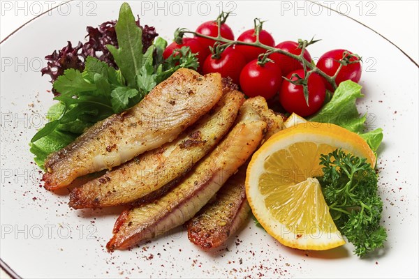 Fried Tilapia fish fillet, in spices, with cherry and salad, on a white plate, homemade, no people