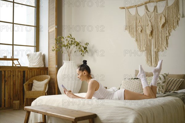 A woman lies comfortably on a bed in a room adorned with natural textures and soft lighting,