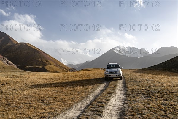 Off-road vehicle on a track between yellow meadows, glaciated high mountain peaks in the