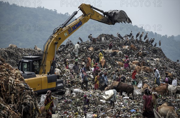 Municipality workers working with excavator as rag pickers searches for recyclable materials next