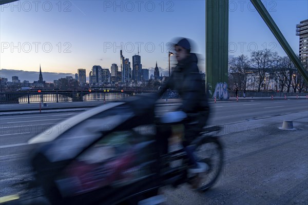 Skyline of the city centre of Frankfurt am Main, cargo bike cyclist on the rafter bridge, dusk,