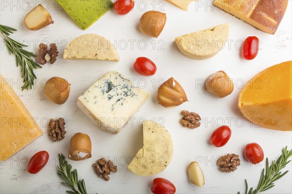 Set of different types of cheese with rosemary and tomatoes on a white wooden background. Top view,