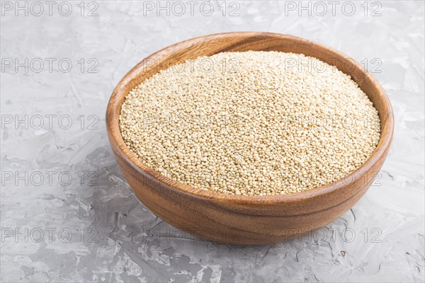 Wooden bowl with raw white quinoa seeds on a gray concrete background. Side view, close up