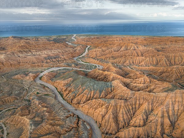 River bed runs through a landscape of eroded hills, badlands, Issyk Kul Lake in the background,