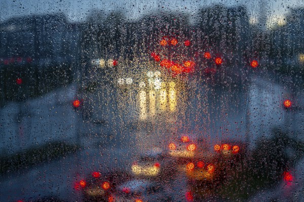Rainy weather, road traffic, raindrops on a window pane, behind, blurred, lights of vehicles on a
