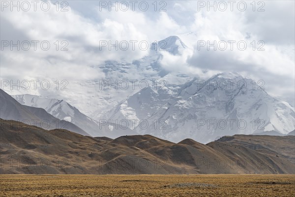 Glaciated, cloud-covered mountain peaks and golden meadows, Lenin Peak, Trans Alay Mountains, Pamir