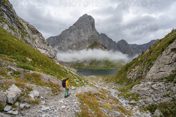 Mountaineer on a hiking trail with a view of rocky, cloud-covered mountains and Wolayersee, hiking
