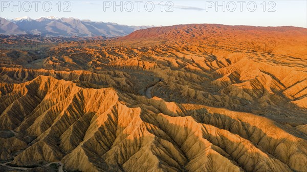 River bed runs through a landscape of eroded hills, badlands at sunset, mountain peaks of the Tian