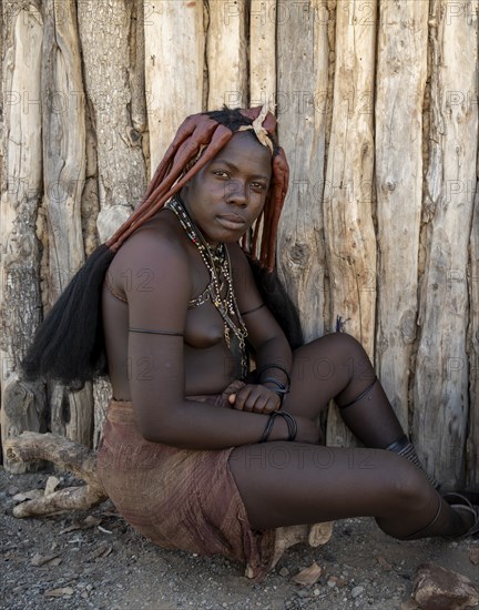 Traditional Himba woman sitting in front of a hut, near Opuwo, Kaokoveld, Kunene, Namibia, Africa