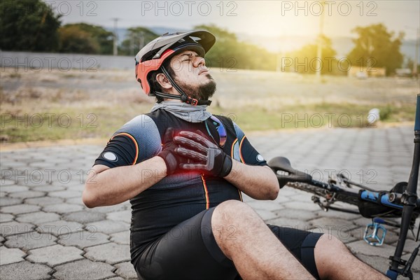 Cyclist on the pavement with chest pain. Concept of cyclist suffering with hand on his chest. Male