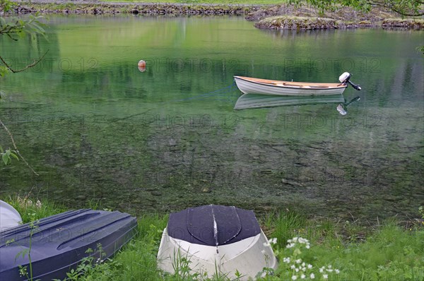 A small boat floats on a calm green lake, surrounded by grass and nature, Mindresundet, Stryn,