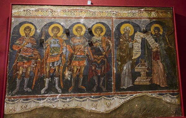 Medieval fresco depicting saints and apostles, all with glowing halos and textual writings on