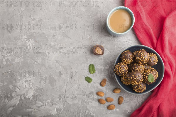 Chocolate caramel ball candies with almonds and a cup of coffee on a gray concrete background and