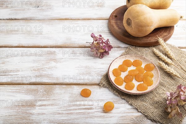 Jelly pumpkin candies on white wooden background and linen textile. copy space, side view. autumn