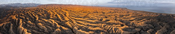 Panorama, landscape of eroded hills, badlands at sunset, Lake Issyk Kul in the background, aerial