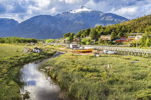 View over swampy meadows, houses and wooden boardwalk of Caleta Tortel, mountains in the back,