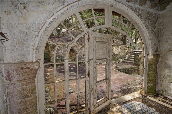 An abandoned building with an arched doorway, broken window panes and broken stone steps, conveying