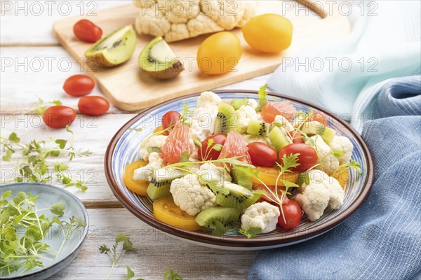 Vegetarian salad of cauliflower cabbage, kiwi, tomatoes, microgreen sprouts on white wooden