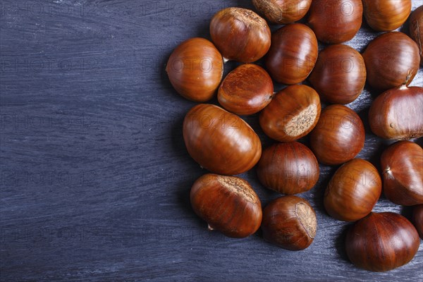 Pile of sweet chestnuts on black wooden background with copy space, top view