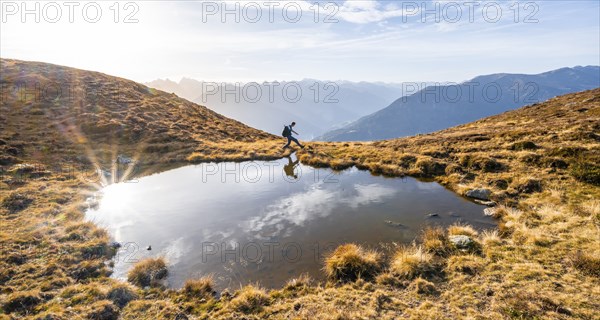 Mountaineer jumping, reflected in a small mountain lake on the Krahberg, mountain panorama in
