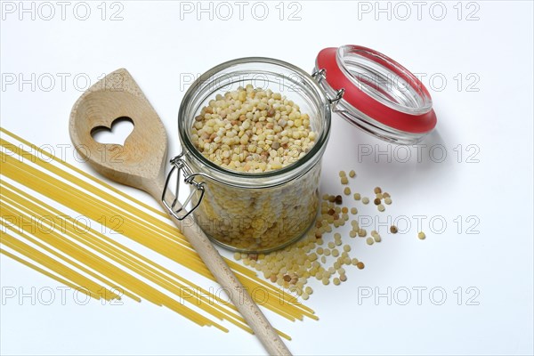 Fregola in wooden spoon and glass container with spaghetti, pasta variety from Sardinia, Italy,