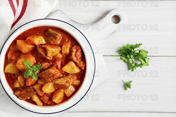 Potatoes stewed with meat, in tomato sauce, with spices and herbs, no people, on a white table
